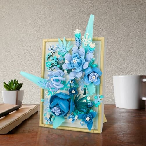 Intricate blue floral art card with paper flowers on a table.