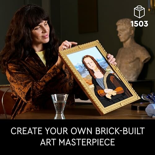 Person holding a framed brick-built artwork resembling a famous painting.