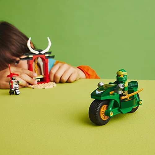 Child playing with LEGO ninja motorcycle set on green background.