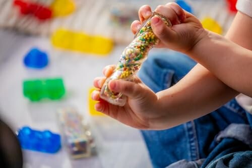 Child holding a colorful sensory toy with blocks in the background.