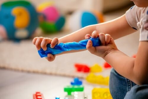 Child playing with a blue twistable toy surrounded by colorful building blocks.