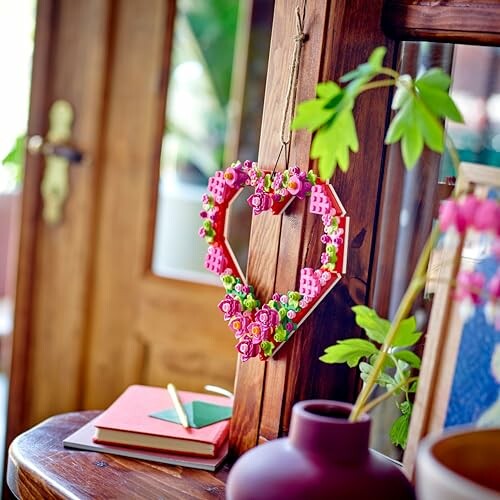 Heart-shaped floral wall hanging with books and a vase on a wooden shelf.