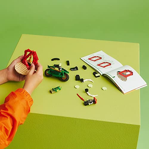 Person assembling a LEGO set with a motorcycle and instruction booklet on a green table.