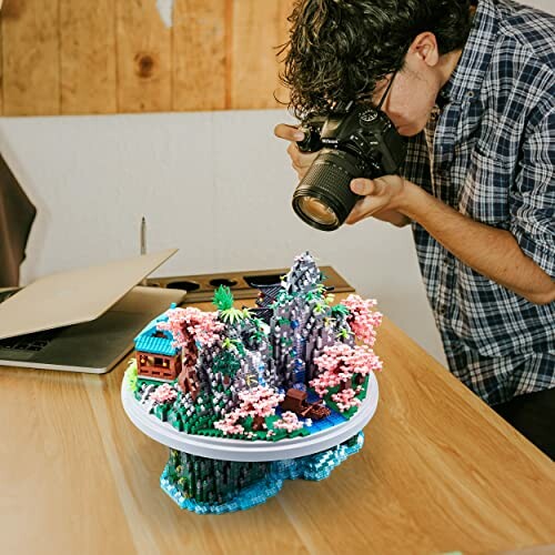 Person taking a photo of a miniature landscape model on a table.