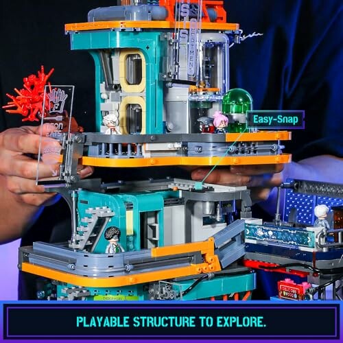 Hands holding a colorful, multi-level toy structure with small figures.