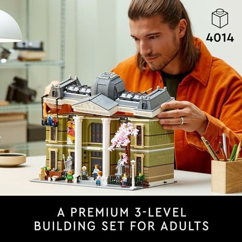 Person assembling a 3-level building set with figures and detailed architecture.