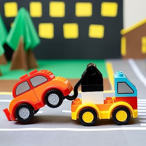 Toy tow truck lifting a small red car made from building blocks.