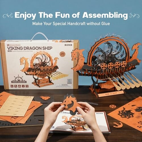 Hands assembling a Viking dragon ship model kit with box and parts.