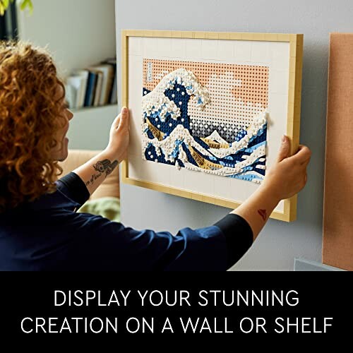 Person hanging framed artwork of a wave on a wall.