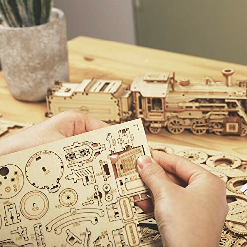 Hands assembling a wooden train model kit on a table.